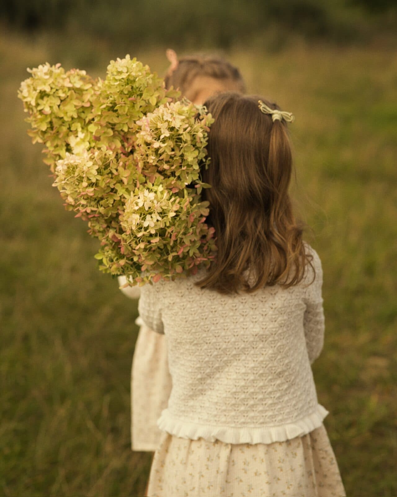 Girl in a white cardigan carrying a bouquet of hydrangeas