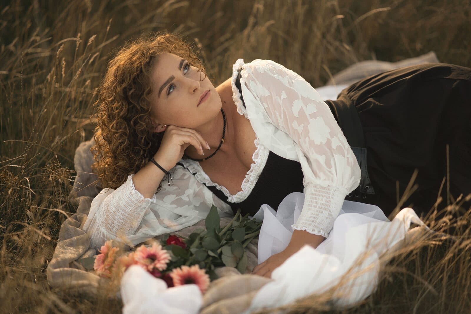 Woman in a white blouse lying in tall grass with a bouquet of flowers